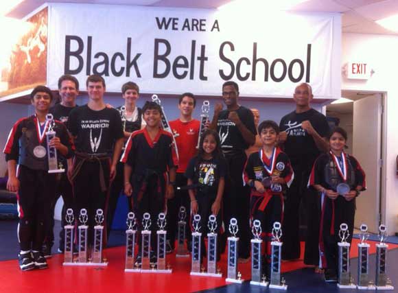 Karate students and teachers with advanced belts and trophies.